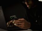 Crop anonymous ethnic male cyber spy with cellphone and netbook hacking system in evening